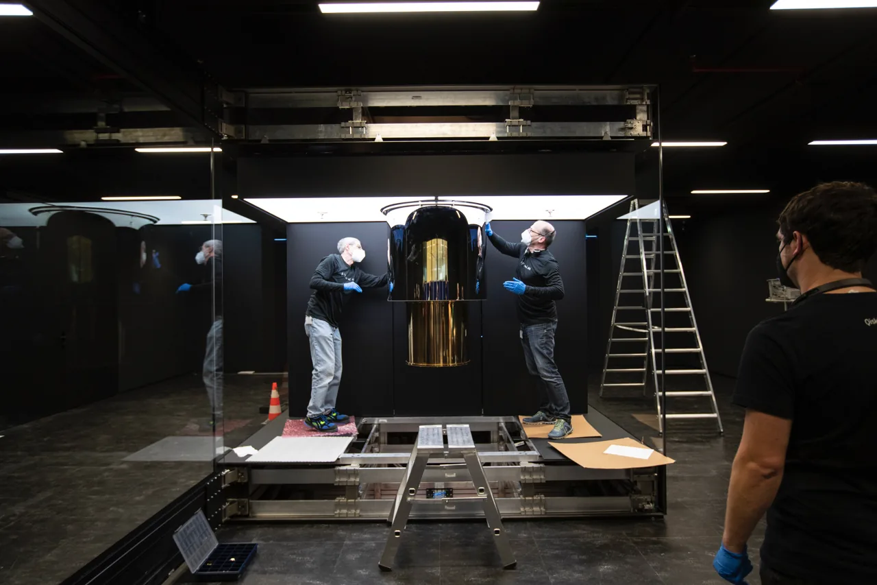 Engineers work beside the gold-colored quantum computing assembly during an IBM Quantum System One installation.