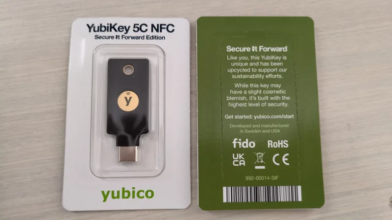 A YubiKey 5C NFC in its original Secure It Forward packaging beside the package back.