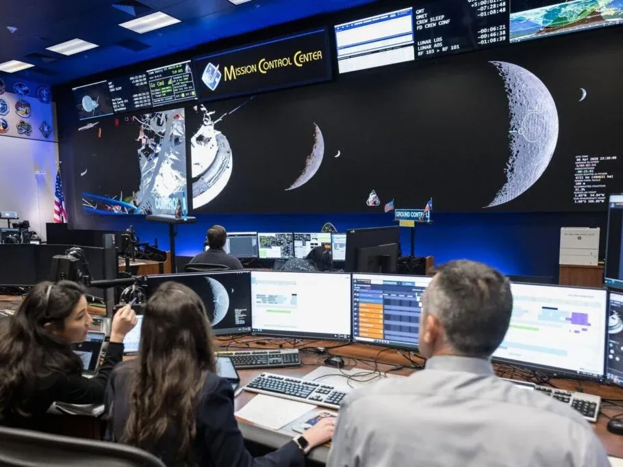 Three science officers monitor computer displays beneath the large screens at NASA Mission Control.