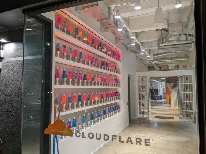 A wall of colorful lava lamps is visible through the Cloudflare office entrance window.